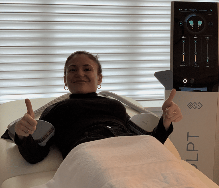 Woman getting EmSculpt treatment on her arms at Manhattan Aesthetics. She is showing two thumbs up.