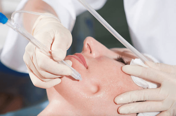 Aesthetician performing a hydrafacial treatment using a handheld device on a woman's face