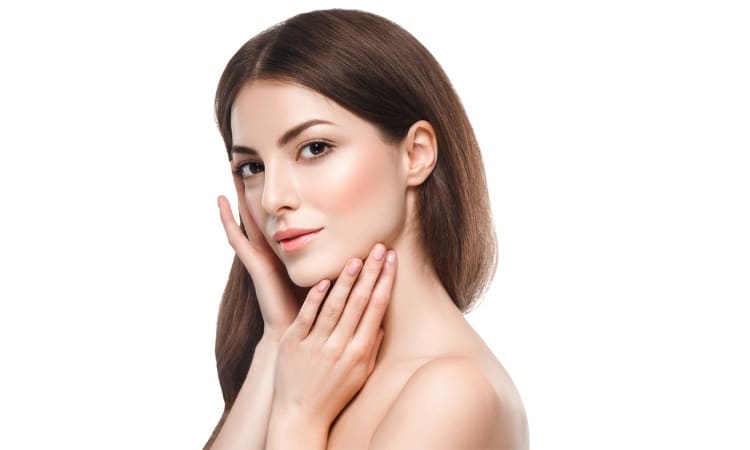 Young woman with clear glowing skin touching her face, posing against a white background