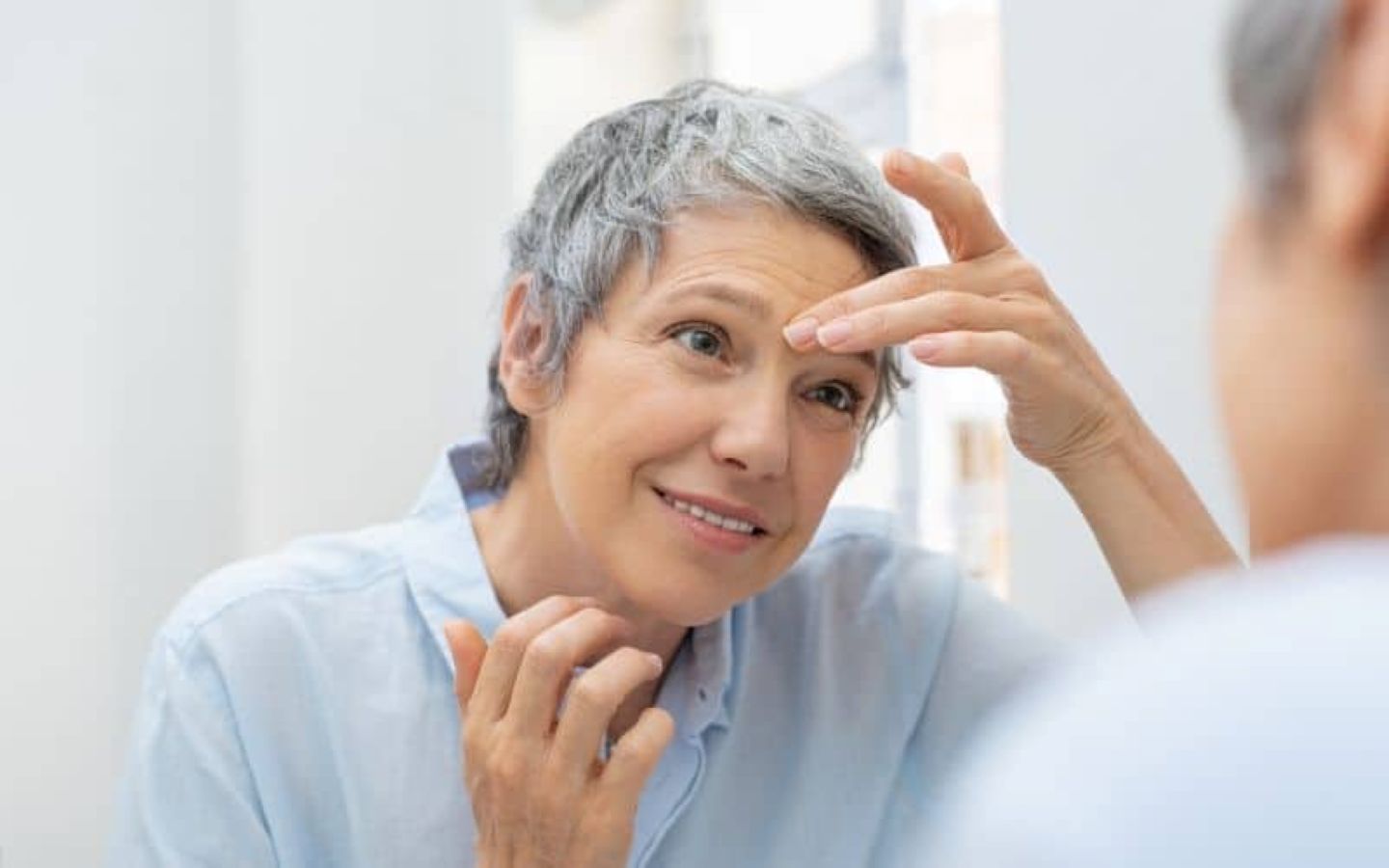 Older woman examining wrinkles on her forehead while looking in the mirror