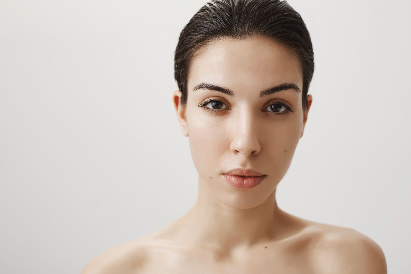 Woman with clear, natural skin looking directly at the camera on a neutral background