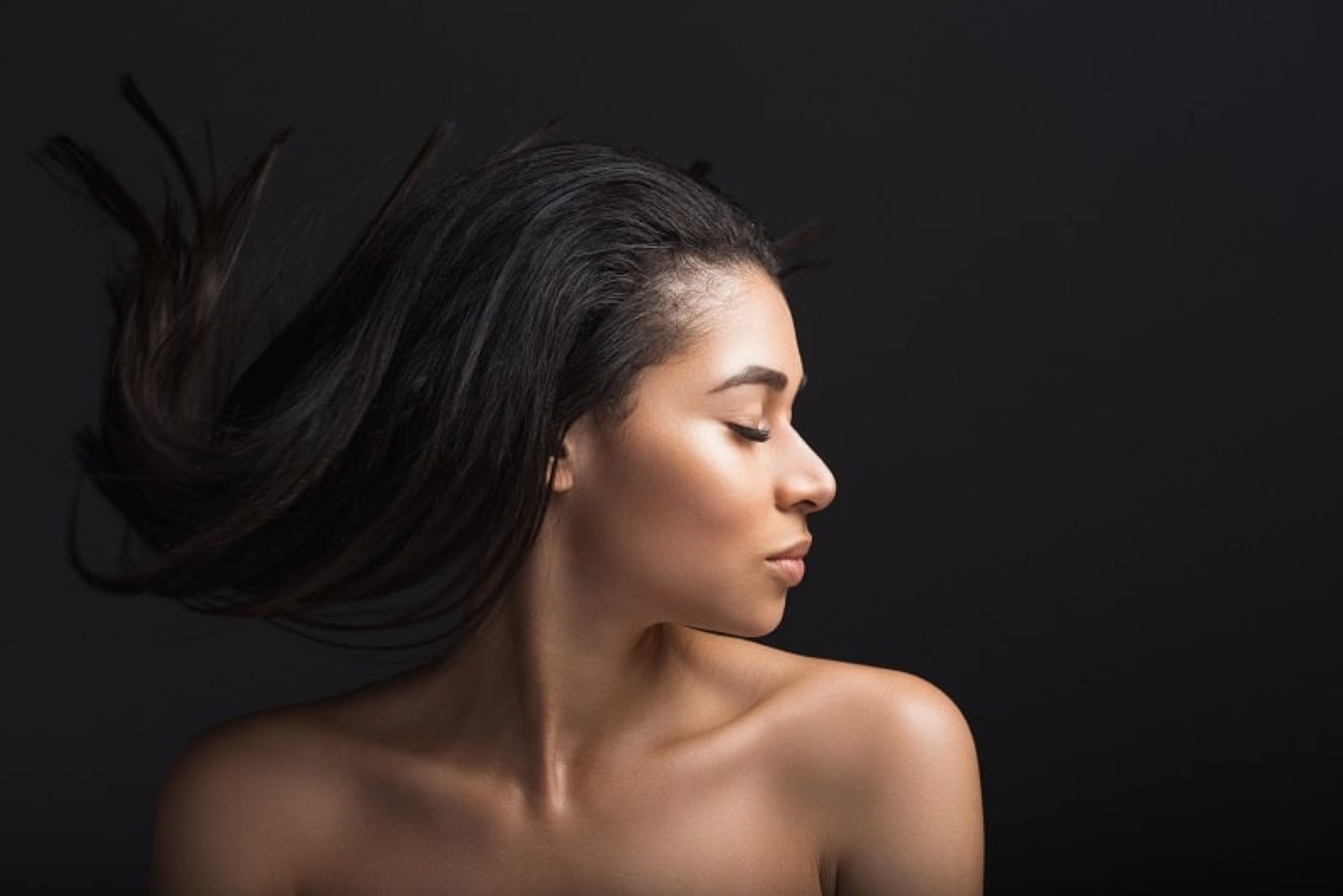 Woman with long hair flipping it back, captured in profile against a dark background.