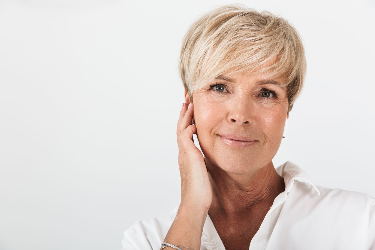 Smiling mature woman with short blonde hair touching her face against a white background