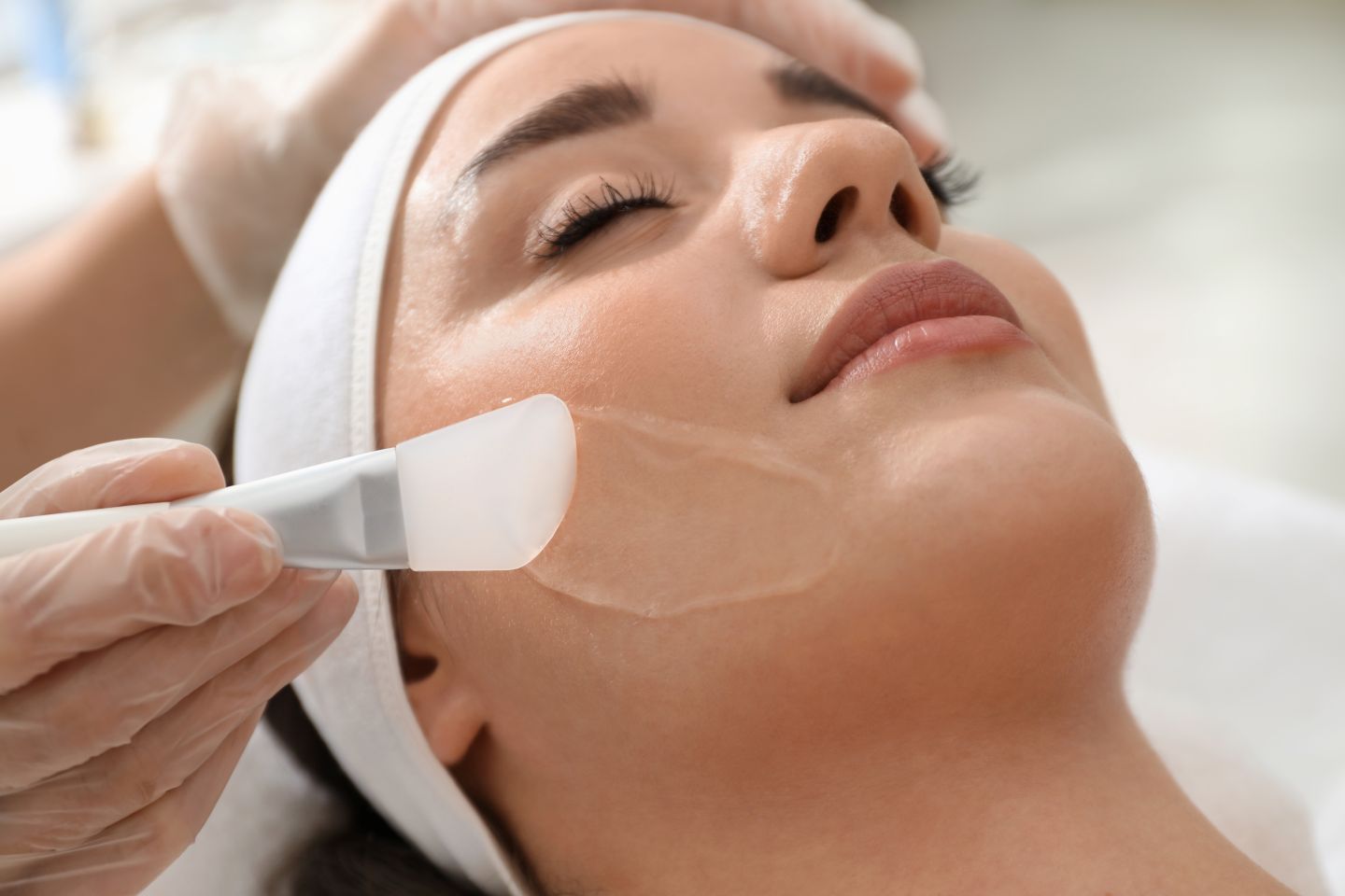 Woman receiving a facial treatment as aesthetician applies gel mask with a spatula